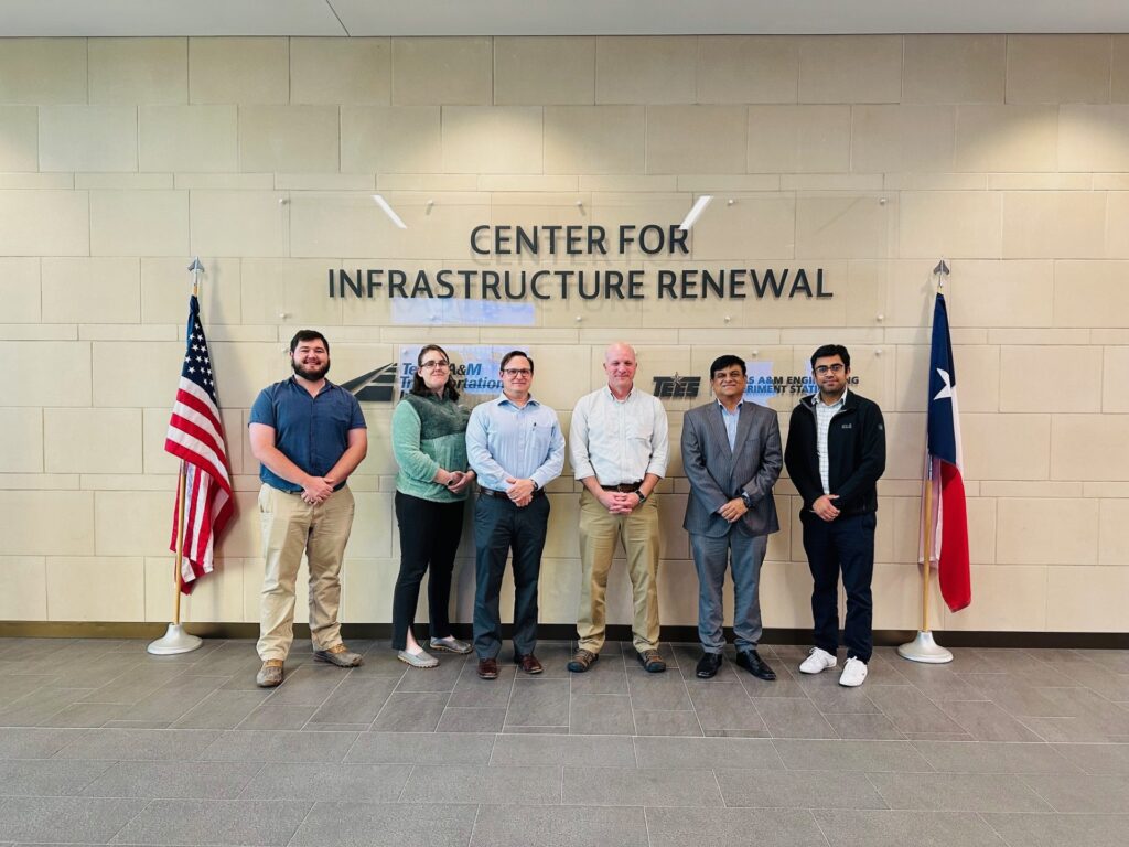 Six meeting attendees standing in front of a wall with a sign