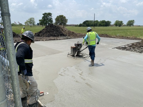 construction workers smoothing and finishing a freshly poured concrete slab.